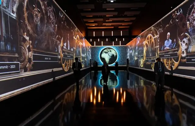 Işıklandırılmış bir koridorun sonunda dünya haritası var. İçeride silüetler görünüyor. 