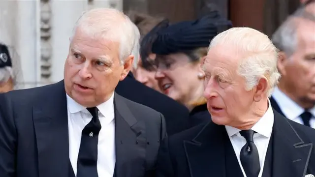 Prince Andrew with his brother King Charles. They are both wearing black suits and ties