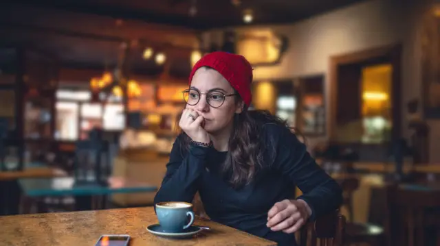 Perempun termangu di kedai kopi dengan ponselnya