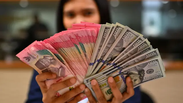 Karyawan memperlihatkan uang pecahan rupiah dan dolar Amerika Serikat (AS) di gerai penukaran mata uang asing Ayu Masagung, Jakarta, Selasa (12/5/2026).