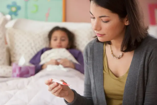 Una mujer comprobando la lectura del termómetro de un niño.