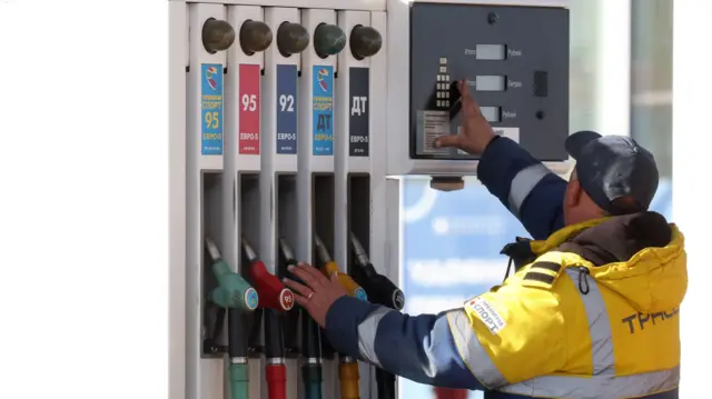 Сотрудник АЗС в Москве в желтой фирменной куртке со светоотражательными полосками стоит у кранов с бензином спиной к объективу