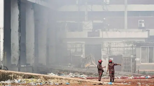 পুড়ে যাওয়া ভবনের সামনে ধোঁয়ার মধ্যে দাঁড়িয়ে একজন ফায়ার ফাইটার আরেকজনকে হাত তুলে কিছু একটা দেখাচ্ছেন