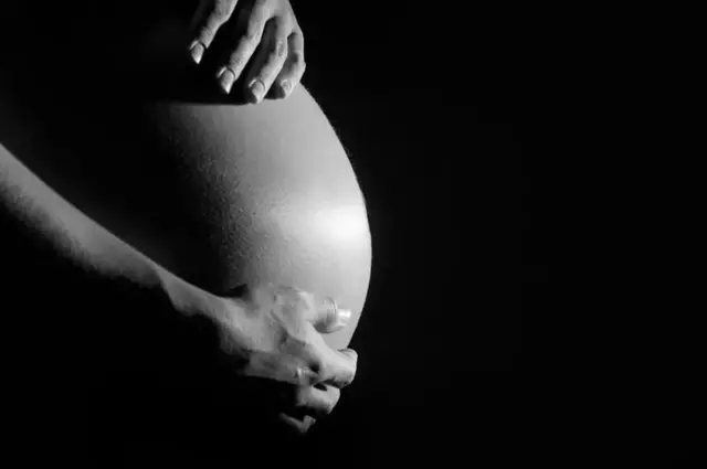عکسی سیاه و سفید از نمای نزدیک شکم زنی باردار در حالیکه دستانش را در بالا و پایین برآمدگی شکمش قرار داده است