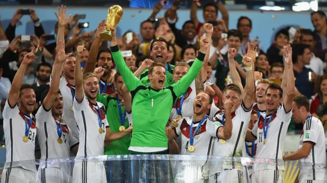 Led by captain and goalkeeper Manuel Neuer, who holds the World Cup trophy and wears a green shirt, Germany team players celebrate their triumph over Argentina in the 2014 tournament. The players are wearing medals around their necks.