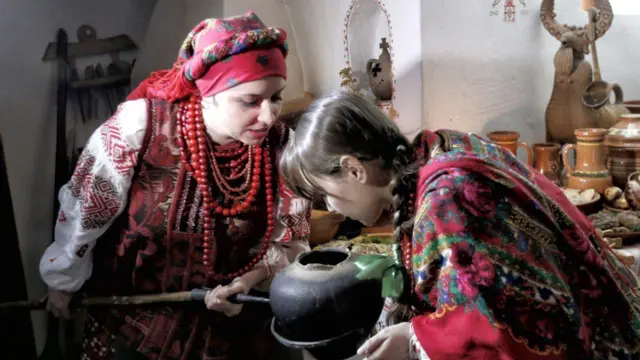 Жінка та дівчинка у національних костюмах дістали з печі казан з кутею 