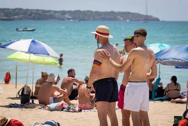 Turyści nakładają krem z filtrem przeciwsłonecznym na plaży Palma w Palma de Mallorca, w tle piaszczysta plaża i morze