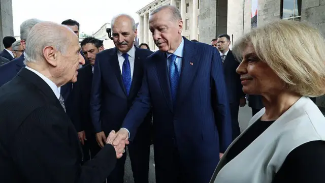 TBMM'deki 15 Temmuz anma etkinliğinde MHP lideri Devlet Bahçeli, Cumhurbaşkanı Erdoğan, TBMM Başkanı Numan Kurtulmuş ve eski başbakan Tansu Çiller aynı karede. Bahçel ve Erdoğan el sıkışıyor, Çiller tebessüm ediyor.
