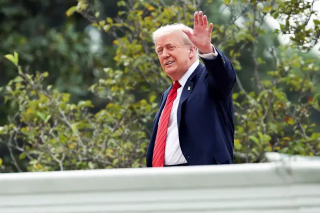 Donald Trump saluda sonriente con la mano izquierda en alto. 