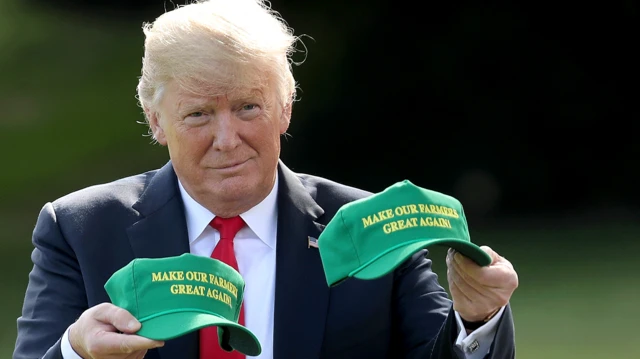 Trump sostiene dos gorras estilo MAGA que dicen Haz a Nuestros Agricultores Grandes Otra Vez 