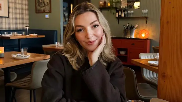 Ginger Smith stă la o masă într-un restaurant, cu o farfurie de stridii și un cocktail în față