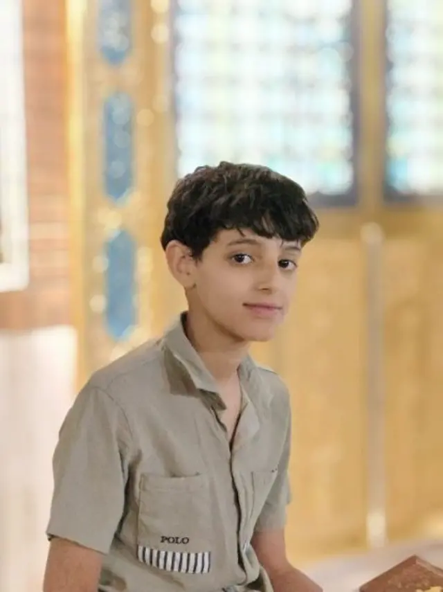 الطفل مهدي من العراق يرتدي قميصاً بنياً