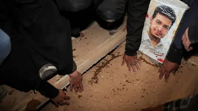 La imagen de un joven que murió en los ataques de Estados Unidos e Israel es colocada sobre su tumba, que acarician con sus manos varias mujeres