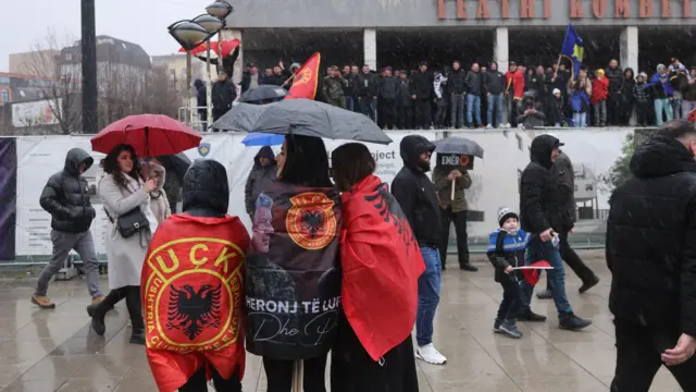 tri devojke ogrnute u albanske zastave i zastave OVK stoje na ulici Prištine