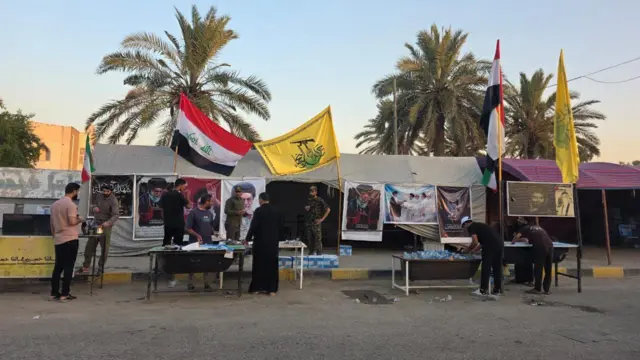 رجال عراقيون يحضرون قوارير مياه للشرب أمام خيمة علقت عليها صور علي خامنئي