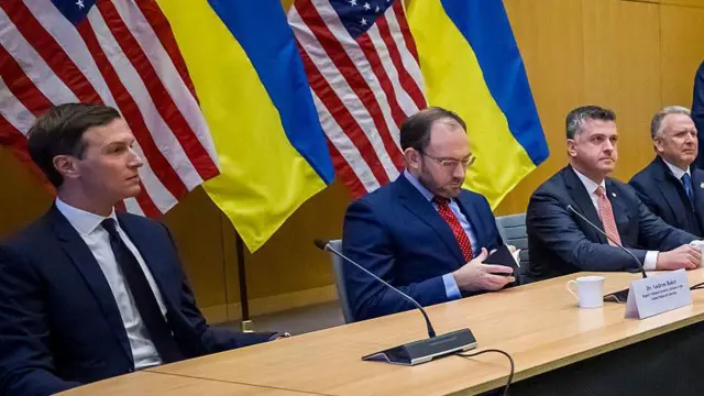 Кушнер и еще три мужчины сидят за столом переговоров на фоне флагов США и Украины.