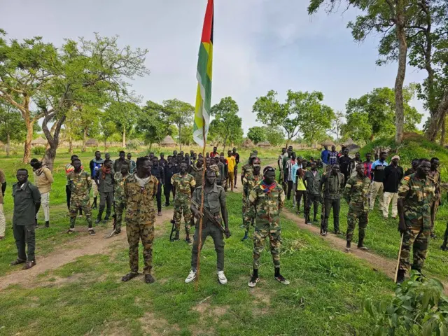 ባንዲራ የያዘን ጨምሮ ወታደራዊ ልብስ የለበሱ ታጣቂዎች ቆመው