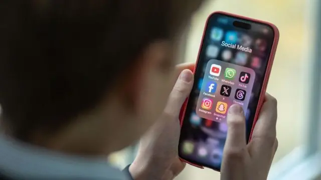 Seorang anak laki-laki berusia 12 tahun melihat ke layar iPhone yang menampilkan berbagai aplikasi media sosial termasuk TikTok, Facebook dan X.