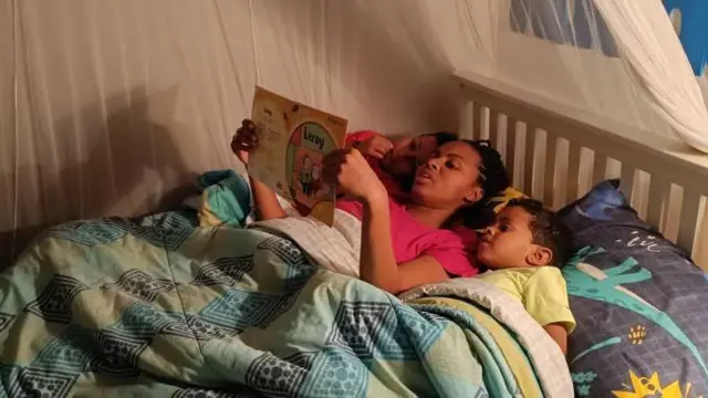 Mulher lendo uma história para dois filhos, deitada entre eles na cama