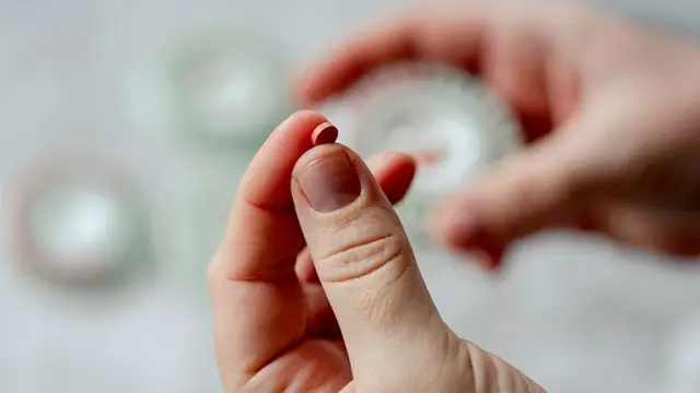 Pessoa com um comprimido em uma das mãos e um recipiente de dosagem desfocado em outra