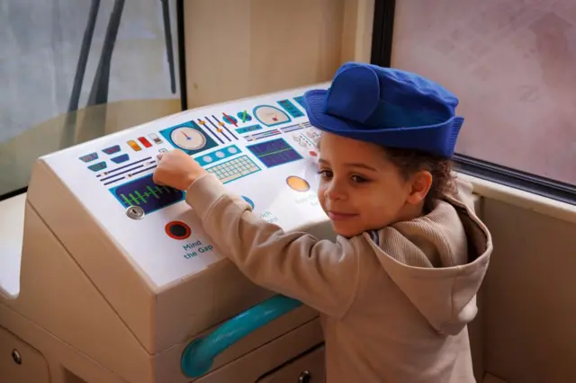 ребенок за передней панелью поезда DLR. На панель нанесена наклейка имитирующая пульт управления поездом. 