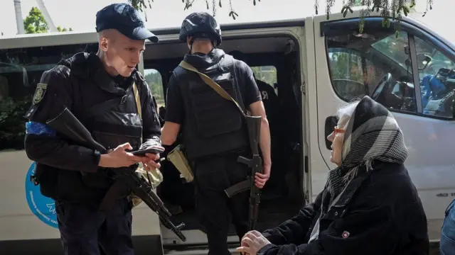 Policial armado conversando com mulher sentada em Vovchansk.