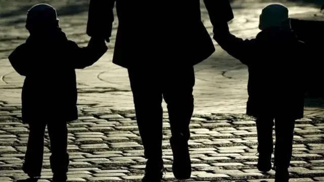 ልጆቹን በግራ እና በቀኝ እጁ ይዞ የሚራመድ አባት 