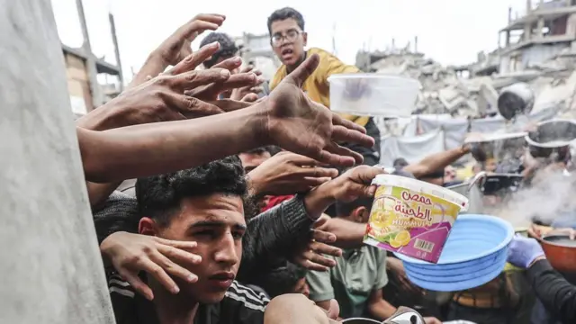 Displaced Palestinians hold out pans at a community kitchen in Jabalia refugee camp, northern Gaza (24 April 2025)