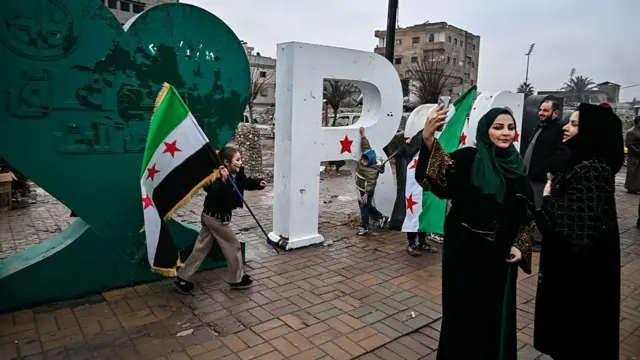 23 Ocak'ta Rakka'da çekilmiş fotoğrafta, kentin Şam'ın denetimine geçmesini kutlayanlar görülüyor. Rakka tabelasının önünde iki kadın selfie çektirirken bir çocuk ise elindeki yeni Suriye bayrağıyla koşuyor.