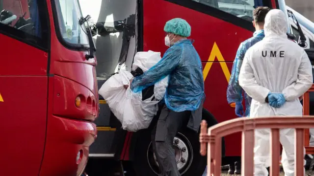Otu onye njem na-ebu ngwongwo ya n'ime akpa plastik gaa na bọs na-eche mgbe a kpụpụrụ ya n’ụgbọmmiri MV Hondius mgbe ọ kwụsịrị n'ọdọụgbọmmiri Granadilla n’ụbọchị Sọnde Mee 10, 2026 na Tenerife dị nso na Canary Islands nke Spen.