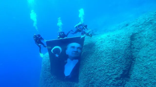 Dalgıçlar, 1968'de bir fırtına sırasında Kaş açıklarında batan Yunan yük gemisi Dimitris'in batık gemisinin yakınında, 19 Mayıs 2025'te Türkiye'nin Antalya kentinde Atatürk posteri ve Türk bayrağı açıyor.