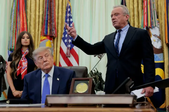 Кеннеди выступает с речью, рядом сидит Трамп