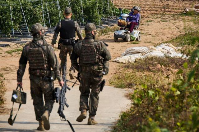 Tres militares de espaldas y, al fondo, Kim Dong-rae en un carrito