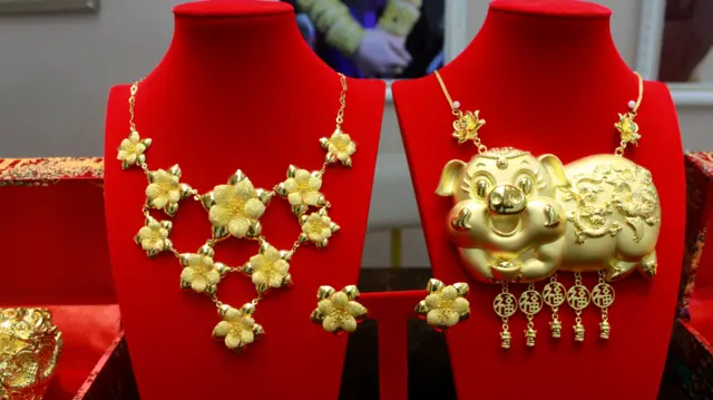 两款金器的近照，左边是花形图案的金项链，右边是金猪牌。