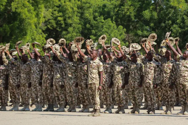 Nigerian troops in military fatigue raising their hats