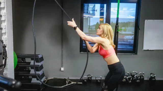 Kobieta w stroju sportowym ćwiczy na siłowni, ciągnąc za linkę na maszynie do ćwiczeń, styl życia sportowca