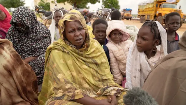 امرأة سودانية تجلس على الأرض في مخيمات النزوح ويحيط بها عدد من النساء والأطفال