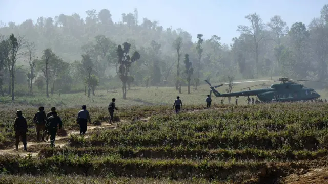 In this photo taken on January 24, 2026, soldiers and police walk towards a military Mi-17 helicopter transporting a military-organised press tour at a drug production site southwest of Mongyai, northern Shan State, that was captured by the Myanmar military.