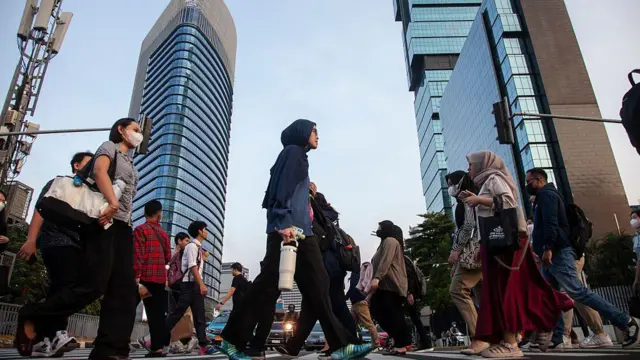 Para pekerja sedang berjalan menyeberangi jalan di Jakarta, pada 11 Juni 2025.  Pemerintah berencana menerapkan WFH untuk menghemat bahan bakar minyak (BBM) pada April 2026. 