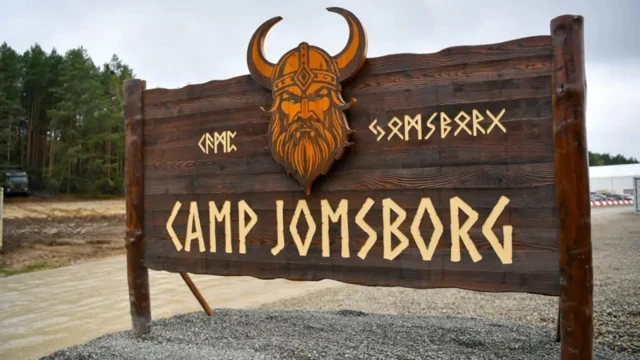 Деревянная табличка с изображением головы викинга в рогатом шлеме, на ней написано «Лагерь Йомсборг» и изображены руны.