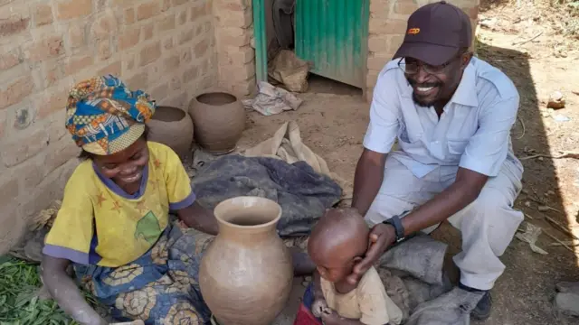 Father Adrien Cishugi is sitting with a pottery maker from the Pygmy community 