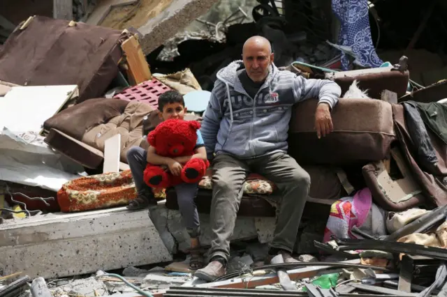 ग़ज़ा में एक घर के मलबे पर बैठे लोग