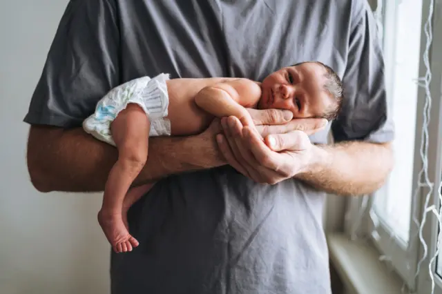 Bir adam yeni doğmuş bir bebeği kollarında tutuyor.