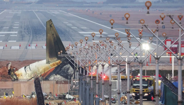 Kaza yapan uçağın ayakta kalan tek parçası olan kuyruğu ve pist aynı karede görülüyor. Uçağın çarptığı ışıklandırma sistemi ve duvar da kadrajda. Etrafa enkaz parçaları saçılmış.