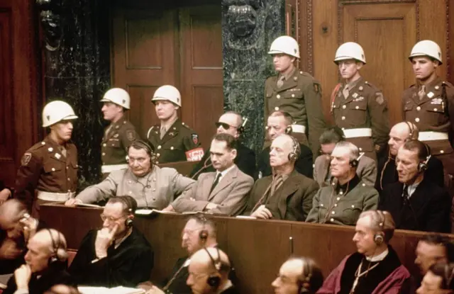 Hermann Goering (ex-chefe da força aérea nazista), Rudolf Hess (ex-vice-chanceler), Joachim von Ribbentrop (ex-ministro das Relações Exteriores) e Wilhelm Keitel (ex-chefe do Exército nazista) na sala de audiências do Palácio da Justiça de Nuremberg, cercados por soldados dos EUA.