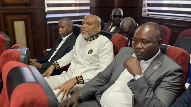 Nnamdi Kanu wear white sidon in-between security operatives wey carry am come court 