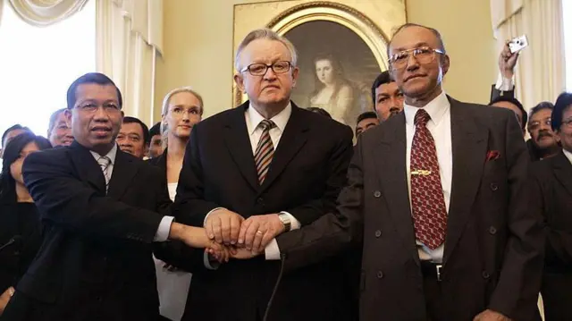 Menteri Hukum dan HAM Indonesia Hamid Awaludin (kiri) dan Ketua Delegasi Perunding Gerakan Aceh Merdeka (GAM) Malik Mahmud (kanan) dan Ketua Dewan Inisiatif Manajemen Krisis Finlandia Martti Ahtisaari berjabat tangan setelah penandatanganan perjanjian damai di Helsinki, 15 Agustus 2005.