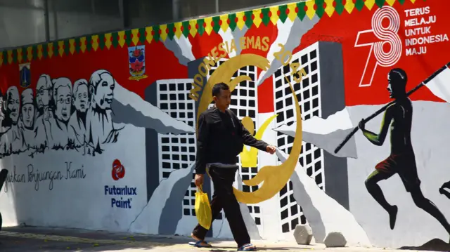 Warga berjalan di depan mural bertema Pemilu 2024 di Jalan Perjuangan Raya, Jakarta, Kamis (28/09).