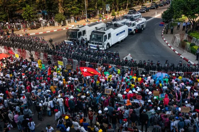 YANGON, MYANMAR - FEBRUARY 09: Riot police and water canon vehicles stand at a barricade as protesters approach them on February 09, 2021 in Yangon, Myanmar.