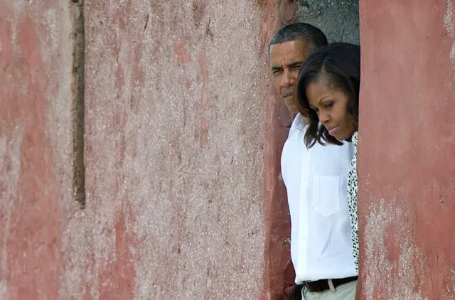 Barack et Michelle Obama à la porte de non-retour, l'ancien président des Etats-Unis porte une chemise blanche et sa première dame une chemise à motif. Ils ont des visages graves.